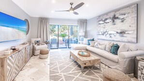 A spacious living room with a large window, a ceiling fan, a sofa set, and a coffee table. - Golf Cart ~ Lake Views ~ Community Pool ~ Patio (Miramar Beach)
