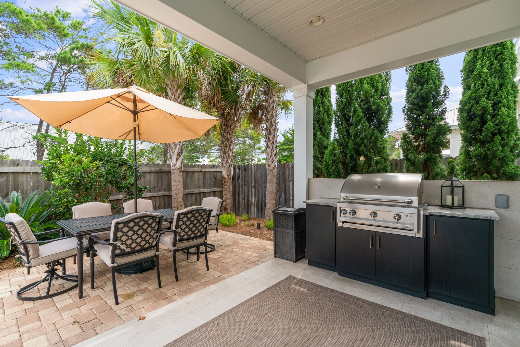 An outdoor kitchen with a grill, dining table, chairs, and an umbrella.