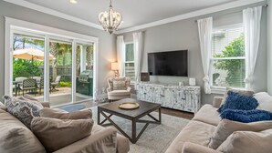 A living room with a sofa, coffee table, TV, and a view of the backyard. - Golf Cart ~ Private Pool ~ Near Beach ~ Grill (Santa Rosa Beach)