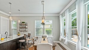 A kitchen with a central island, wooden chairs, a dining table, pendant lights, and a window with curtains. - Golf Cart ~ Private Pool ~ Near Beach ~ Grill (Santa Rosa Beach)