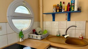 A compact kitchen with a sink, a window, and a blue shelf holding various items. - T2 40 m2 Anse Mitan - Panorama bay of Fort-de-France (Les Trois-Îlets)