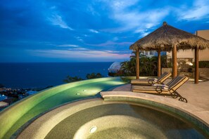 A infinity pool with a view of the ocean, lounge chairs, and a thatched gazebo. - Luxury 5 BR Ocean View Villa del Mar w/ Heated Pool, Home Theatre Room + More (Cabo San Lucas)