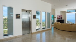 Een ruime woonkamer met een groot raam, een schuifpui en uitzicht op zee.