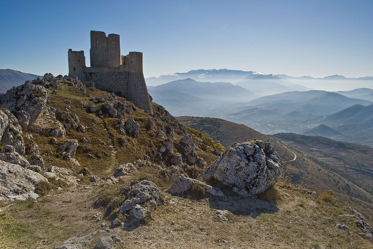 A historic stone castle on a mountain peak with a panoramic view of the surrounding landscape.