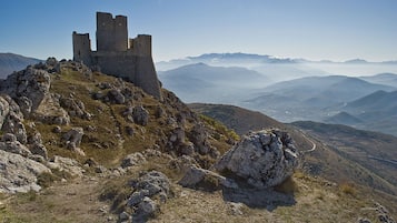A historic stone castle on a mountain peak with a panoramic view of the surrounding landscape.
