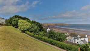 A coastal view with a grassy hill, a pathway, and buildings near the beach. - Belle House, Apt 2 (Filey)