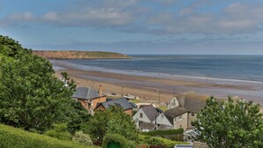 A coastal town with a sandy beach, houses with sloped roofs, and a cliff in the background. - Belle House, Apt 3 (Filey)