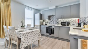 A modern kitchen with grey cabinets, a herringbone-patterned backsplash, and a dining area with a table set for two. - Belle House, Apt 3 (Filey)
