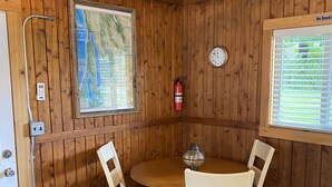 Ett rum med träpanel på väggarna, ett runt bord och fyra stolar, en brandsläckare, en väggklocka och en karta.