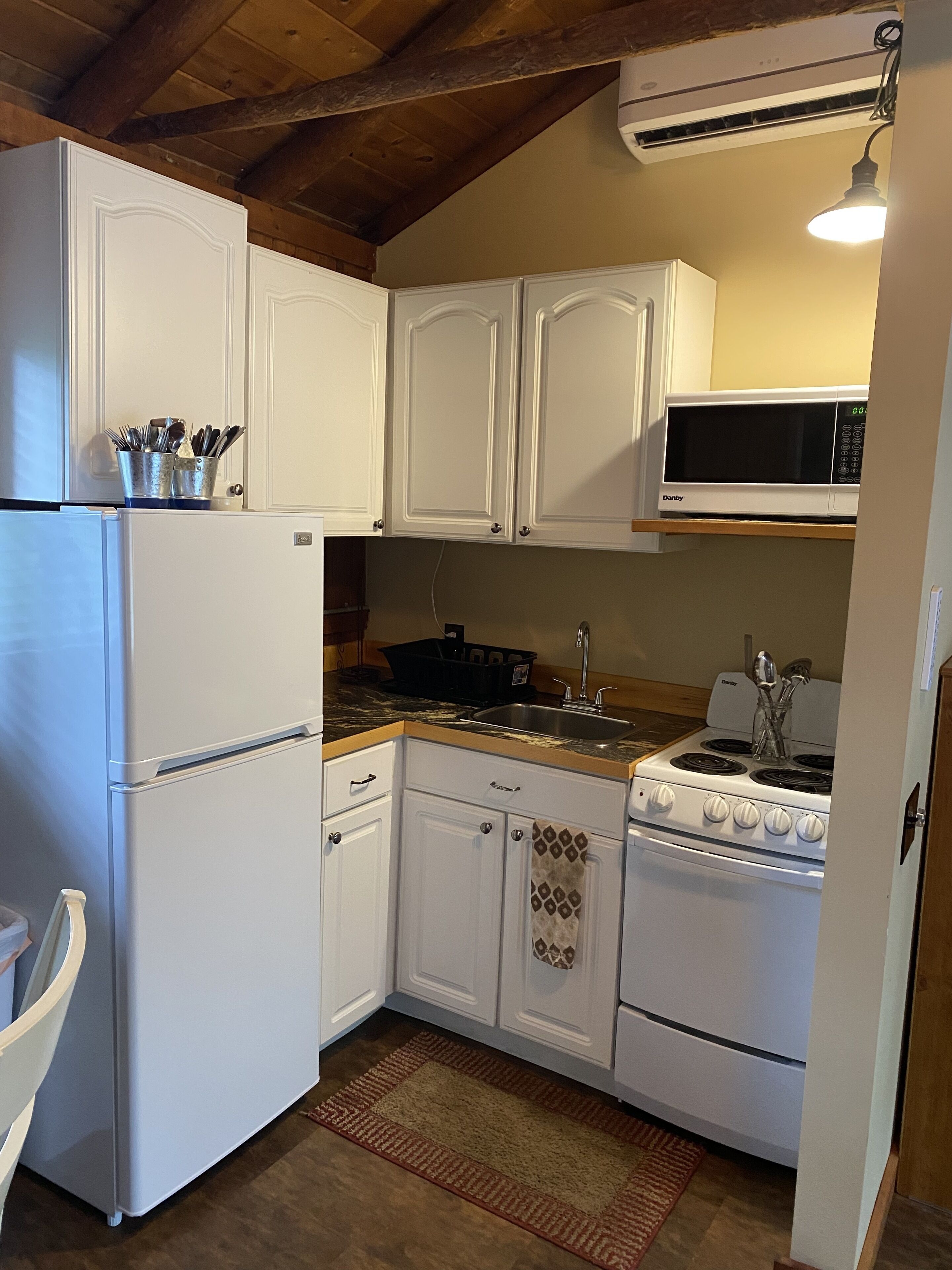 Una cocina compacta con muebles blancos, microondas integrado, estufa y refrigerador.