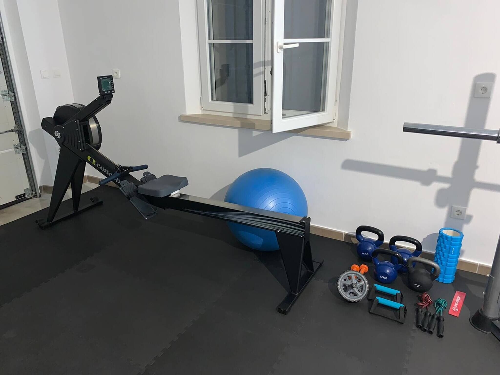 A home gym with a rowing machine, exercise ball, kettlebells, and resistance bands.