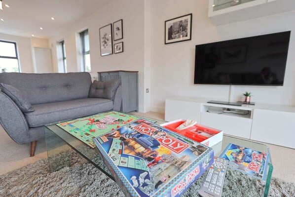 Uma sala de estar com sofá, mesa de centro com jogos de tabuleiro, televisão de tela plana e um armário branco.