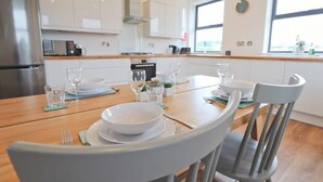 Une cuisine moderne avec des meubles blancs, des appareils en acier inoxydable et une table à manger pour quatre personnes.