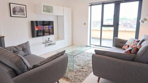 Un salon moderne comprenant un canapé, une table basse en verre, un téléviseur à écran plat et une porte-fenêtre coulissante donnant sur un espace extérieur.
