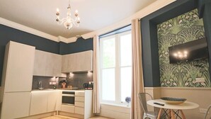Eine moderne Küche mit weißen Schränken, ein Essbereich mit einem runden Tisch und ein großes Fenster mit Vorhängen.