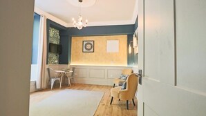 Ein modernes Wohnzimmer mit Holzboden, einem weißen Teppich, einem beigen Sessel, einem Esstisch mit Stühlen und einer Pendelleuchte.