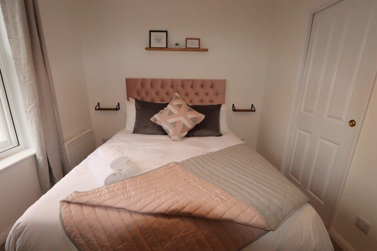 A neatly made bed with a tufted headboard, a bedside shelf with two framed pictures, and a window with curtains.