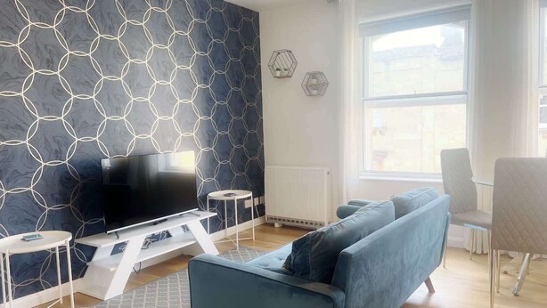 Ein modernes Wohnzimmer mit einem großen Fernseher, einem blauen Sofa und einem weißen Couchtisch.