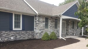 A house with stone exterior walls, a grey roof, and a front porch. - 6 Bedroom house on 7 acres (Sheboygan Falls)