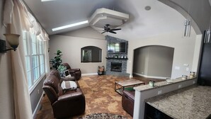 A spacious living area with a ceiling fan, a fireplace, a kitchen island, and a large window. - 6 Bedroom house on 7 acres (Sheboygan Falls)