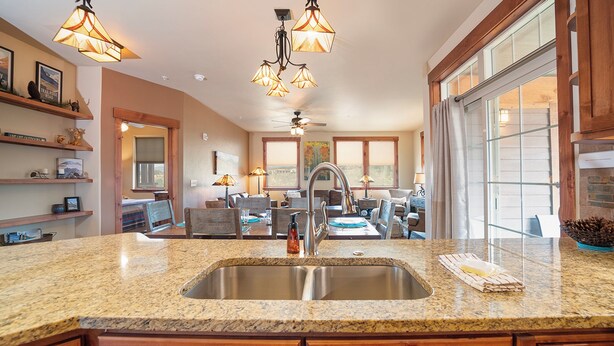Una cocina con encimeras de granito, pileta de acero inoxidable, muebles de madera e iluminación colgante.