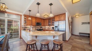 Una cocina moderna con armarios de madera, una isla grande con taburetes, un refrigerador e iluminación colgante.
