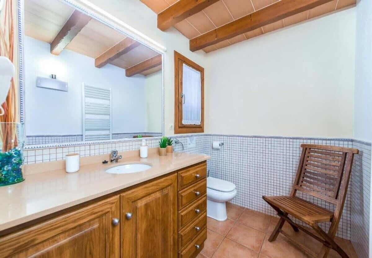 Een badkamer met een houten wastafelmeubel, een wastafel, een spiegel, een toilet en een houten stoel.