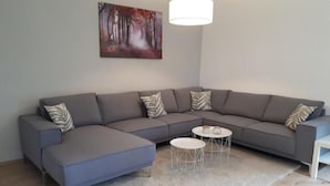 Un salon moderne avec un canapé d’angle gris, deux petites tables rondes et un tableau accroché au mur.