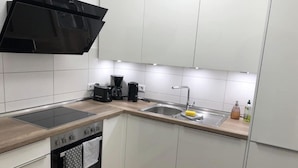 Une cuisine moderne avec des meubles blancs, une hotte noire, un four encastré, un évier et une machine à café.