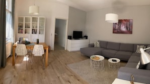 Un salon moderne avec un canapé gris, une table à manger en bois et des chaises, un téléviseur et une bibliothèque.