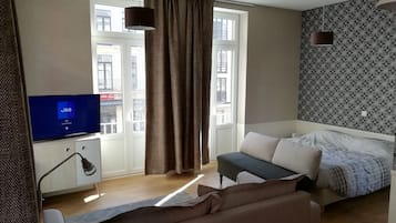 Ett modernt sovrum med en säng, en soffa, en tv och ett fönster med gardiner.