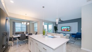 A modern kitchen with a central island, dining area with chairs, a refrigerator, and a TV in the living room. - BE307  Storey Lake Condo 2 bed 2 bath  Free Waterpark (Kissimmee)