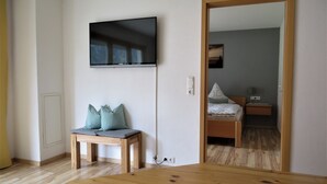 Une pièce comprenant une table en bois, un banc avec des coussins, un lit avec un oreiller, une table de chevet et un téléviseur fixé au mur.