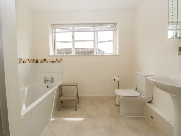 A small, clean bathroom with a bathtub, toilet, and a small step stool. - Tom's Barn (Yeovil)