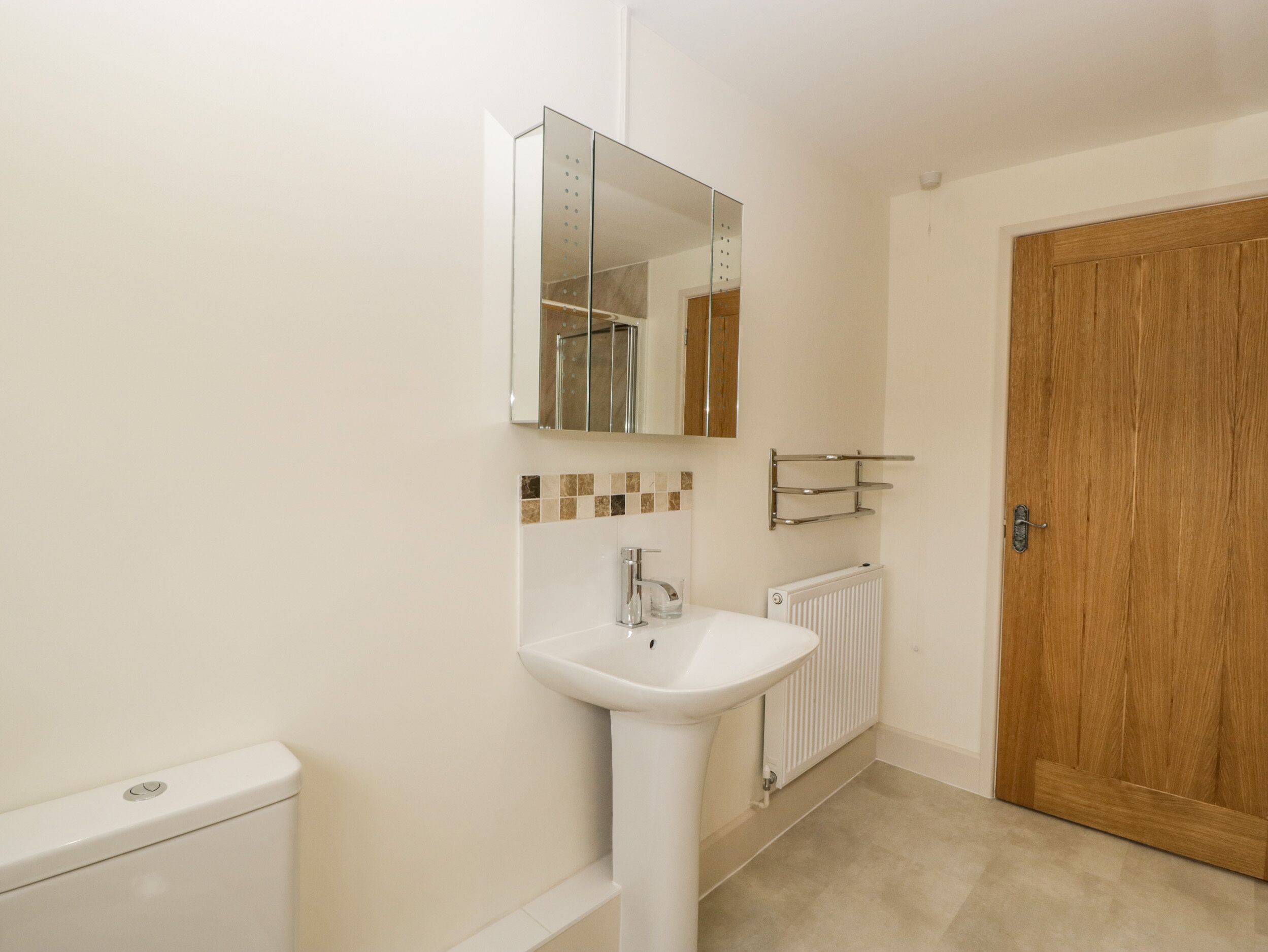A bathroom with a white sink, a mirror, a toilet, and a wooden door.