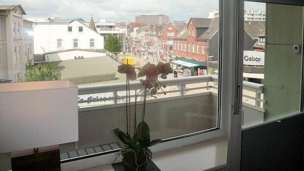 A view from a window with a striped curtain, overlooking a street with buildings and a sign that reads "Gabor".