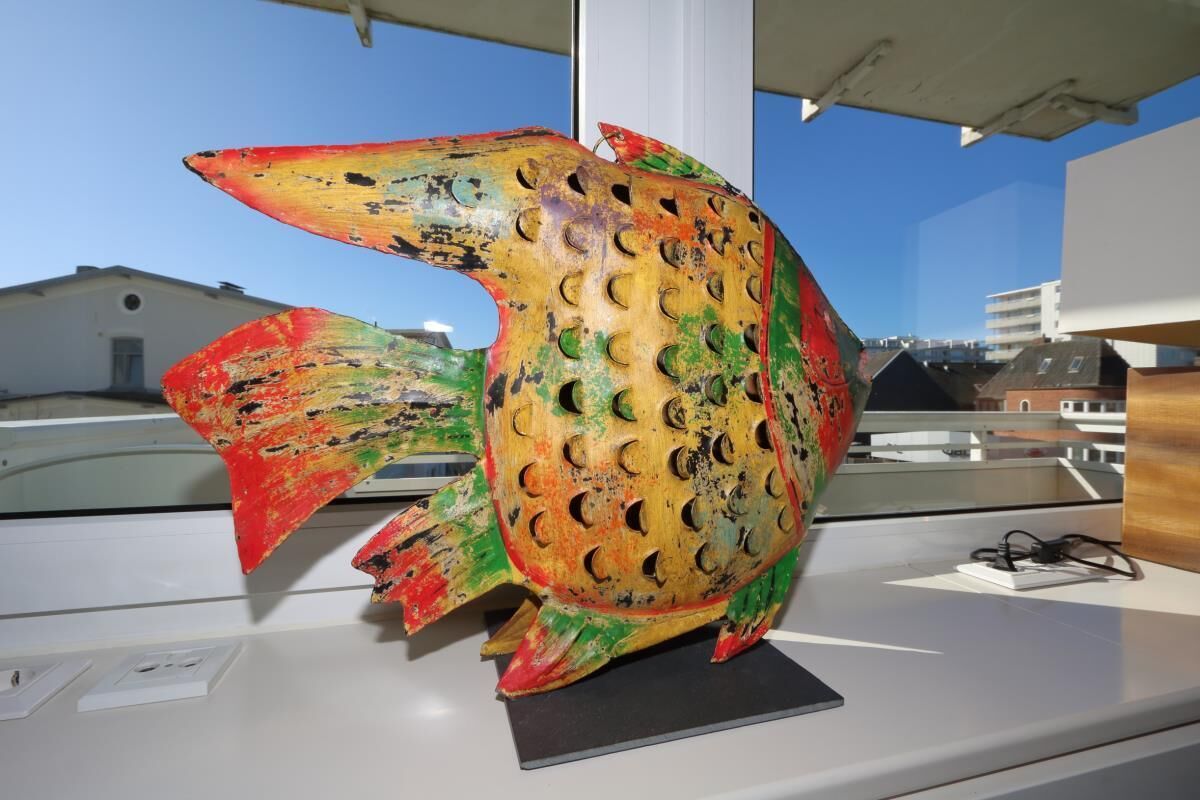 A colorful fish sculpture on a display table with a clear view of buildings in the background.