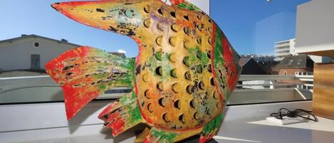 A colorful fish sculpture on a display table with a clear view of buildings in the background.