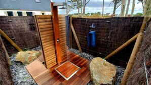 A private outdoor shower area with a wooden door, a small wooden platform, and a blue water tank.