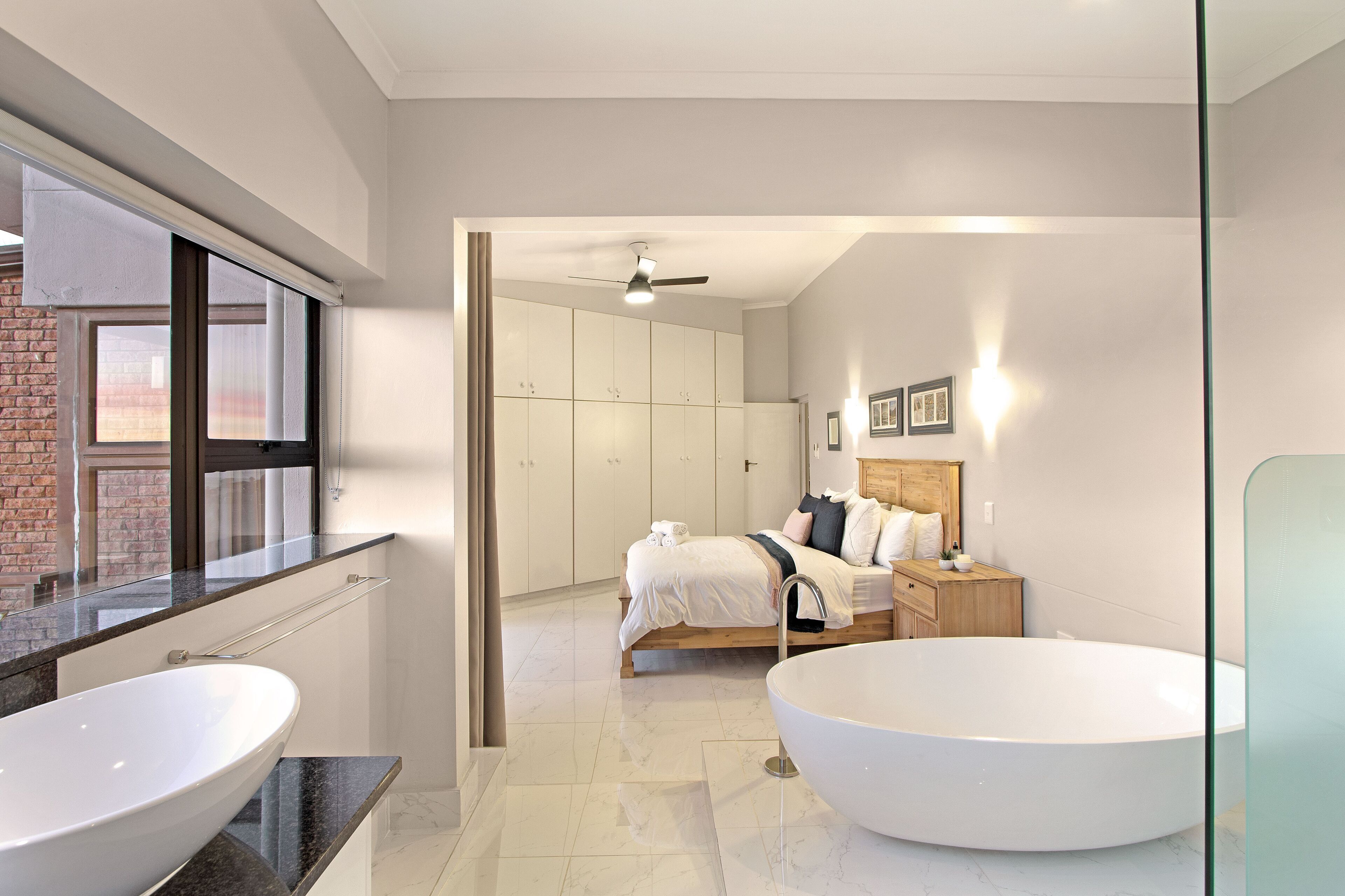 A modern bathroom with two large white sinks, a freestanding bathtub, and a ceiling fan.
