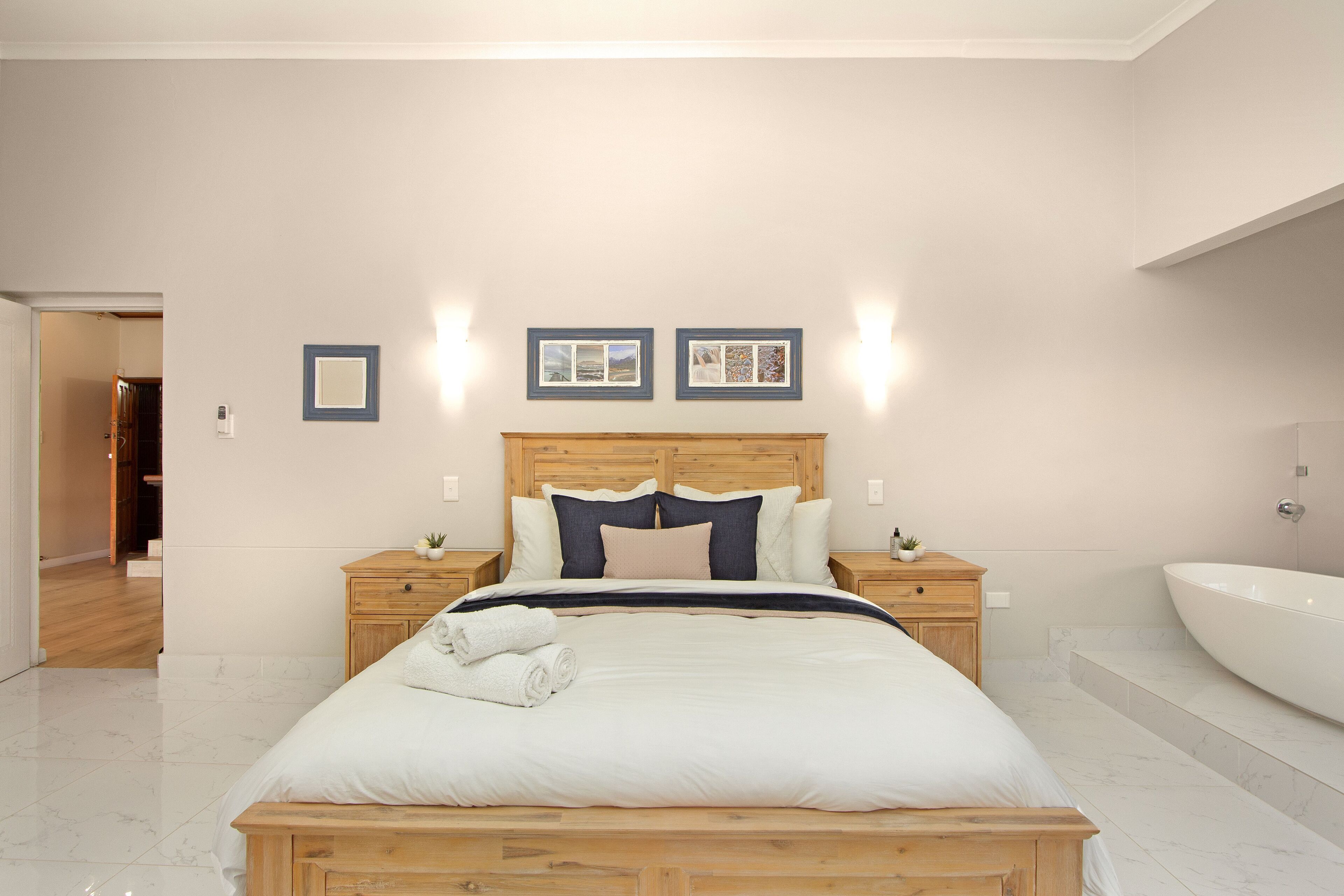 Un dormitorio con una cama de madera, ropa de cama blanca, dos mesitas de noche, un tocador y un baño con bañera.