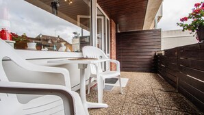 Een terras buiten met een tafel en stoelen, een houten omheining en een gebouw op de achtergrond.