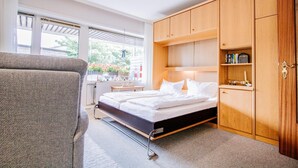 Een slaapkamer met een bed, een houten kledingkast en een raam met uitzicht op groen.