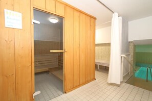 A sauna room with wooden walls, a bench, and a tiled floor. - Ornum, Apt. 2 <br>Location:<br>The "Ornum" house, featuring a sauna and a pool, is located in the center of Westerland, just a short walk from the Wilhelmstraße pedestrian zone, which connects to Friedrichstraße. The beach is about 600 meters away. The Ap (Westerland)