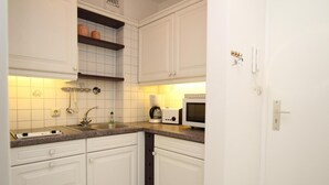 A compact kitchen with white cabinets, a built-in microwave, a coffee maker, and a sink.