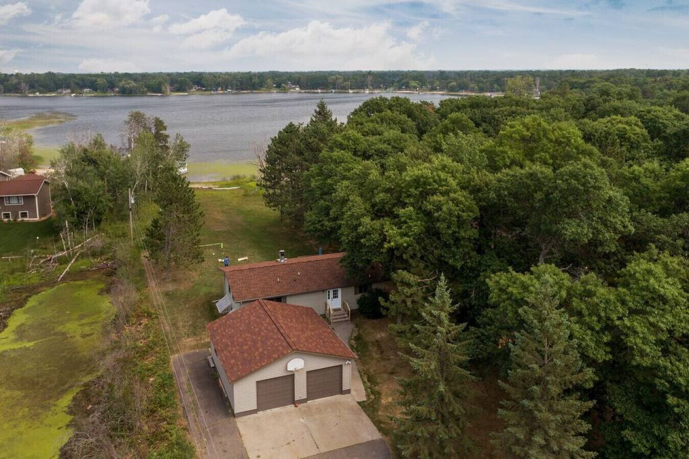 Une maison avec un garage, entourée d’une forêt dense et d’un lac.