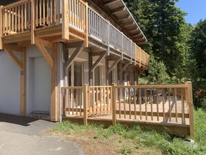 A wooden deck with a railing, a door, and a staircase leading to an upper level.