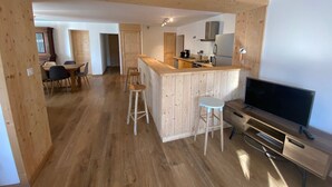 A modern kitchen with wooden accents, a dining area with a table and chairs, and a TV in a corner. - Appartement Rocher du Cerf T5 (Le Lioran)