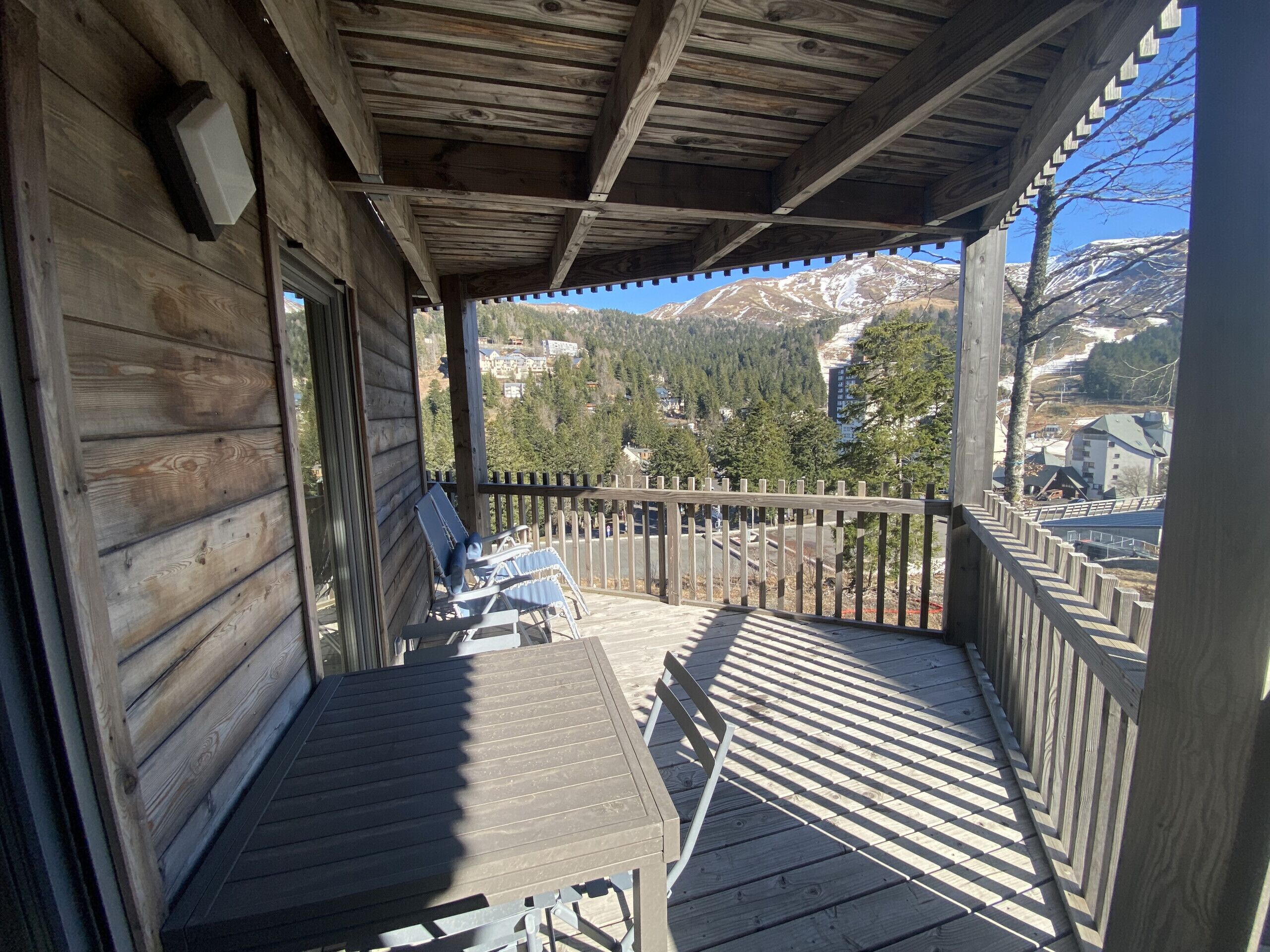 A wooden deck with two lounge chairs, a wooden railing, and a view of mountains and buildings in the background.