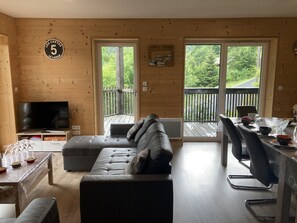 Ein Holzhütten-Interieur mit einer Couch, einem Fernseher, einem Esstisch und großen Fenstern.